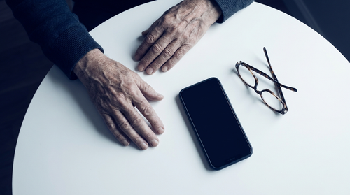 Les mains d'une personne âgée posées à côté de son smartphone